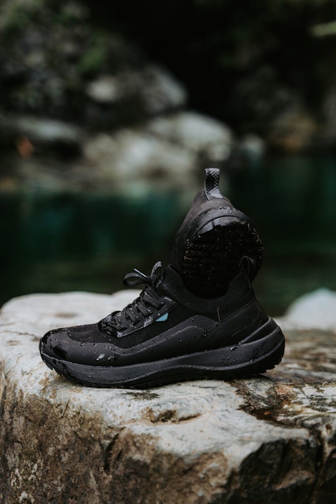 Black hiking shoe with water droplets on a rock by a stream in nature.